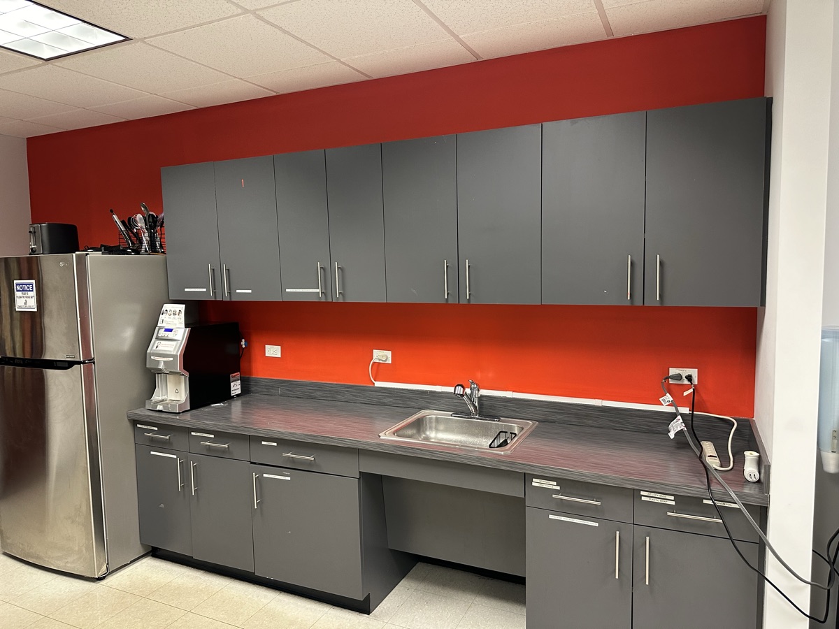 Office kitchenette with red accent wall and gray cabinets