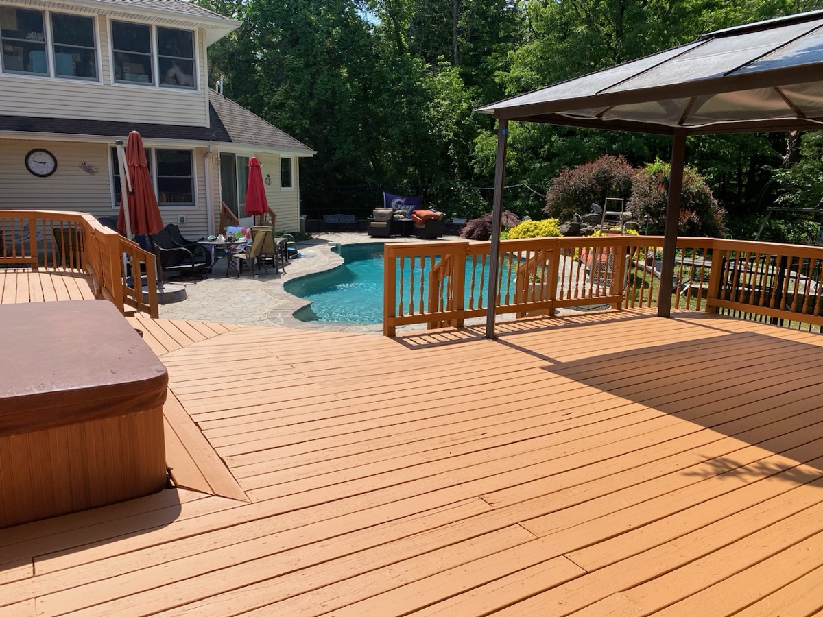 Stained poolside deck with hot tub and pergola