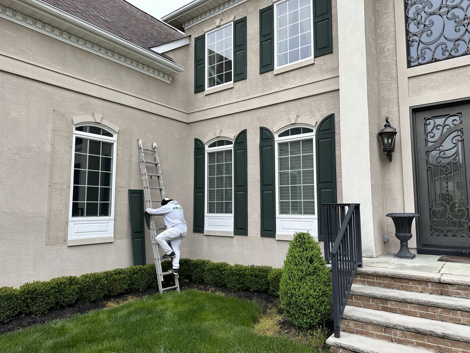 Painter on ladder working on upscale stucco home exterior